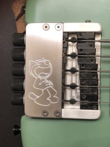 The silver bridge of a guitar with a cartoon character drawn into it