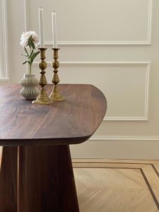 Image of modern dark wood table set with two golden candlesticks and a white vase with a pink flower