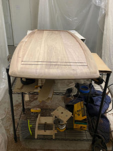 Image of a makeshift workshop with plastic sheets draped around a metal rack holding woodworking tools and a curved wooden table top. 