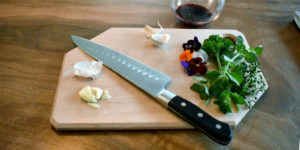 Cutting board with knife, garlic, greens, and wine.