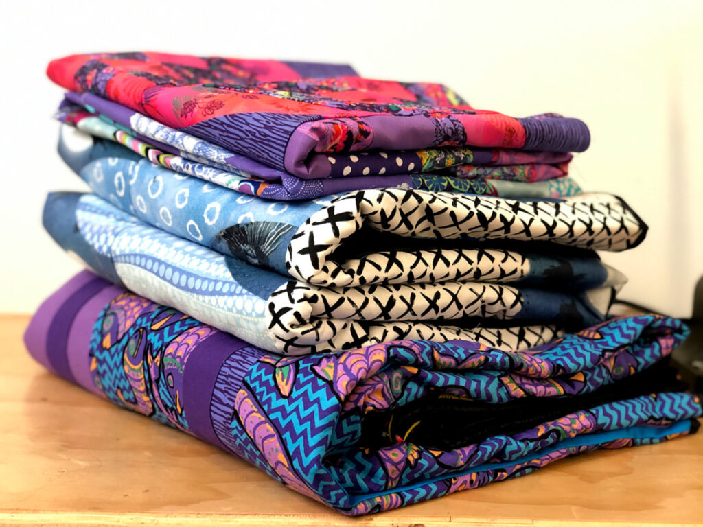 Stack of pink, purple, and blue quilts.