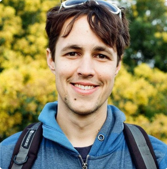 Person in blue hoodie, with sunglasses on head smiling outdoors