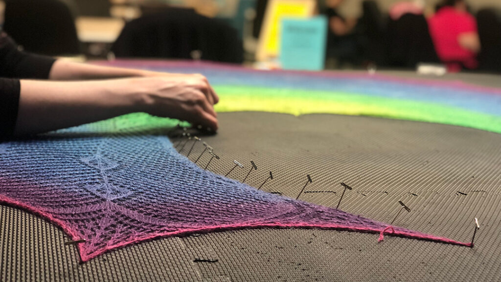 Person knit blocking rainbow shawl