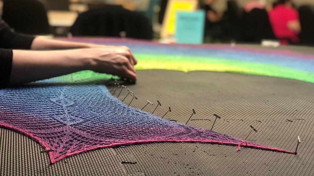 Person knit blocking rainbow shawl
