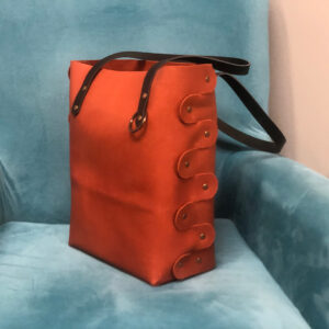 Leather tote bag with brass rivets on a blue velvet chair.