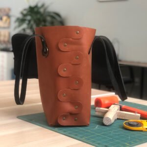 Leather tote bag with brass rivets and leather working tools on a green mat