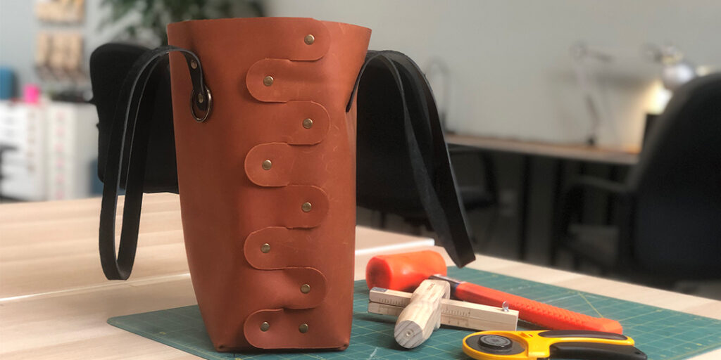 Leather bag with rivets and leather working tools on a green cutting mat