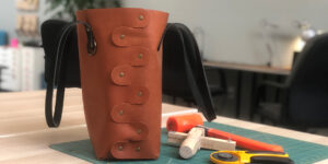Leather bag with rivets and leather working tools on a green cutting mat