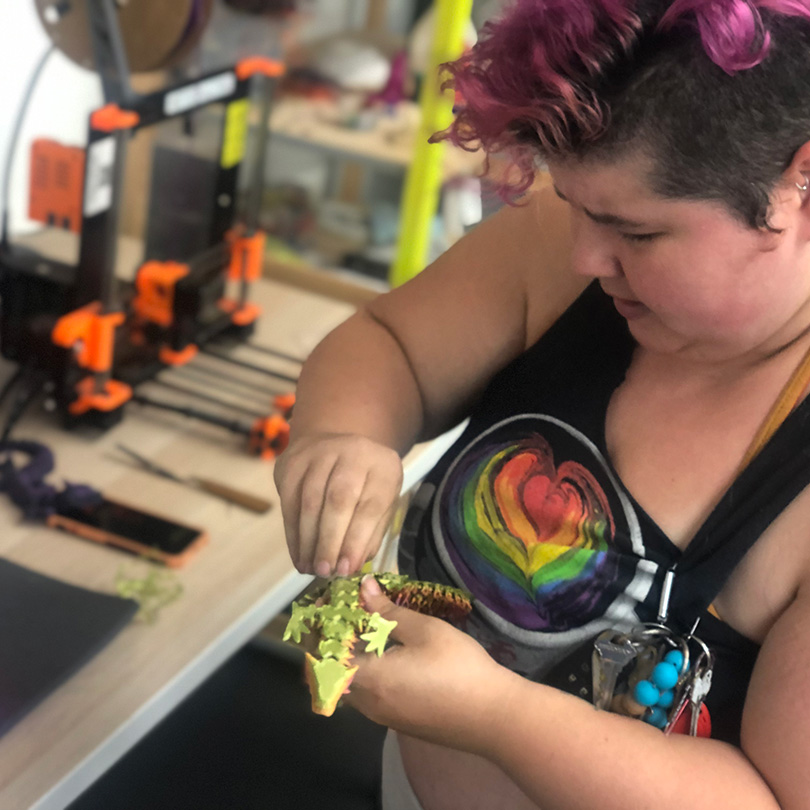 Person removing brim from 3D printed dragon.