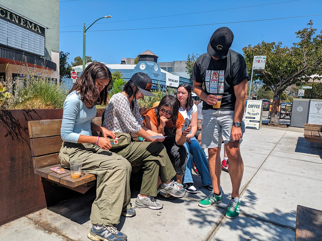 Group sits on bench outside. 