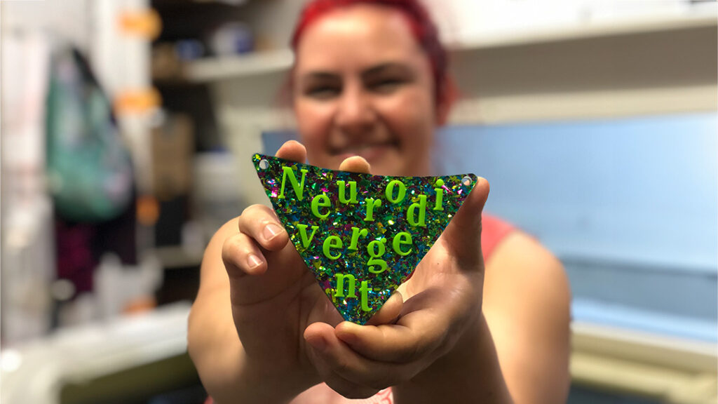 Person holding neon green "neurodivergent" pendent.