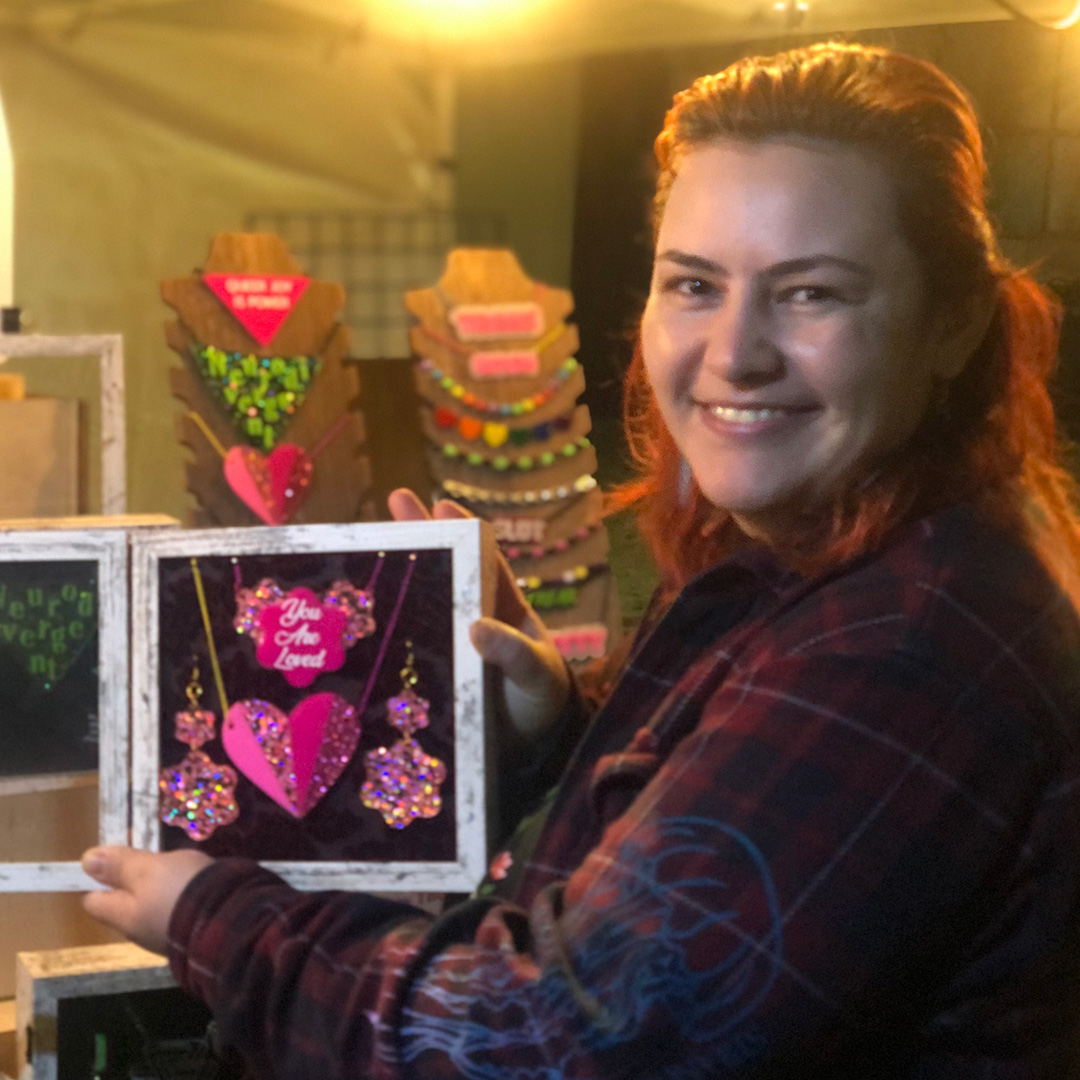 Person smiles with shadow box full of pink laser-cut acrylic jewelry. 