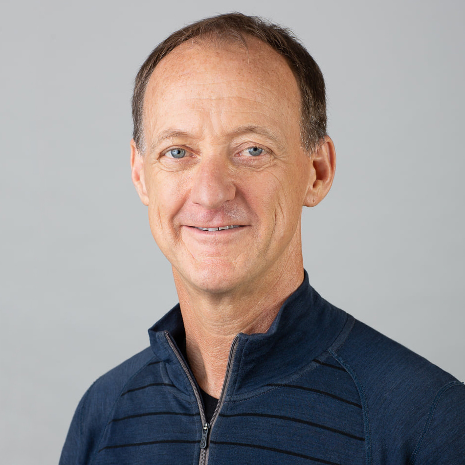 Headshot of person with blue sweater looking at camera and smiling, gray background