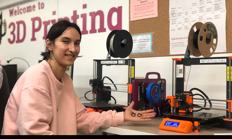 Person holding 3D Printed kitty rings in front of 3D printes.