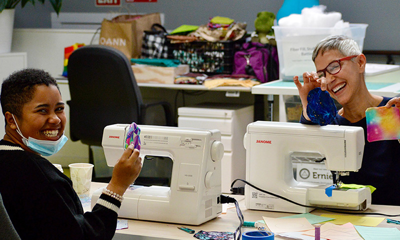 Two students smiling with sewing machines.